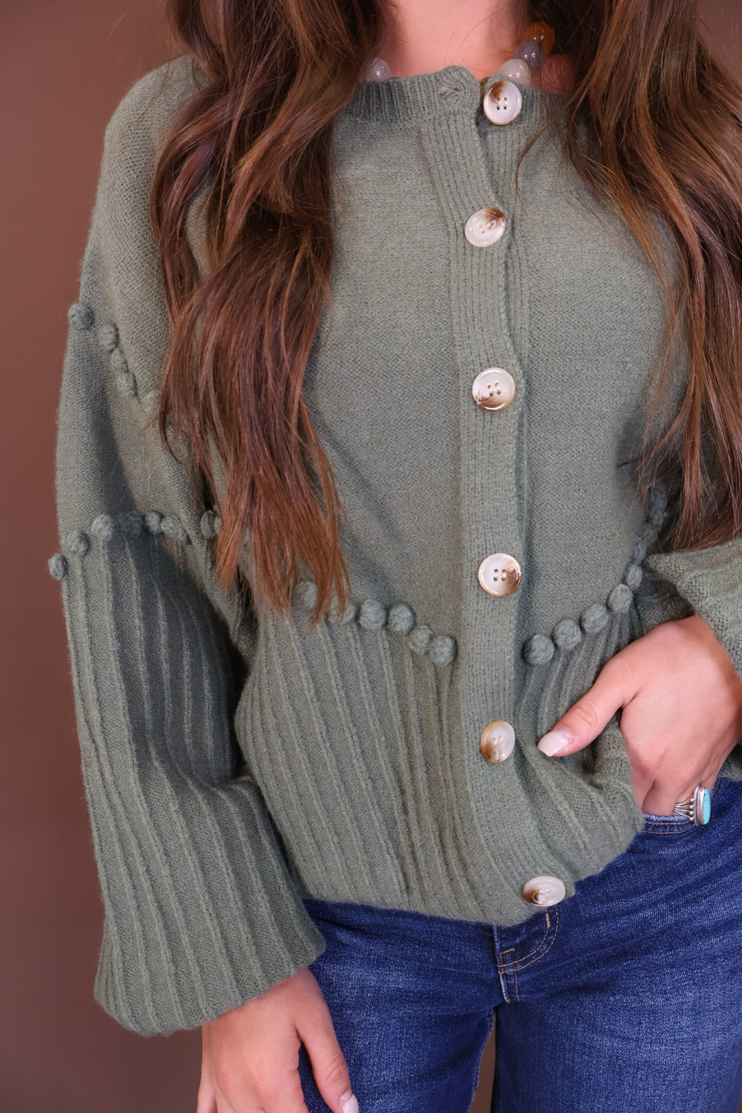 Olive Pom Pom Knit Cardigan — close-up of buttons, pom pom trim, and ribbed knit.