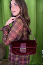 Burgundy plush shoulder bag with rectangular buckle detail.